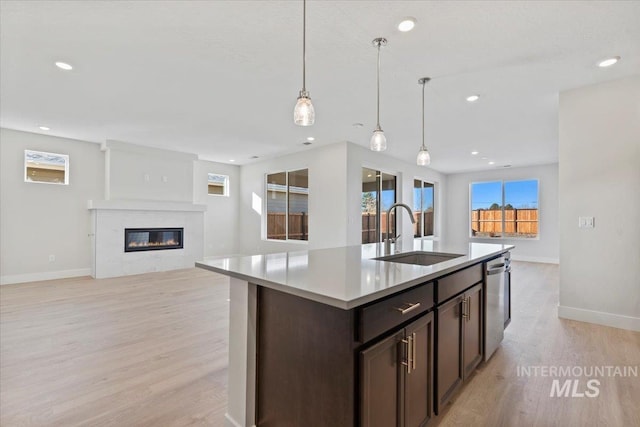 kitchen with sink, dishwasher, hanging light fixtures, a center island with sink, and light wood-type flooring