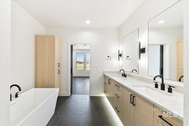 bathroom featuring a freestanding bath, double vanity, a sink, and tile patterned floors