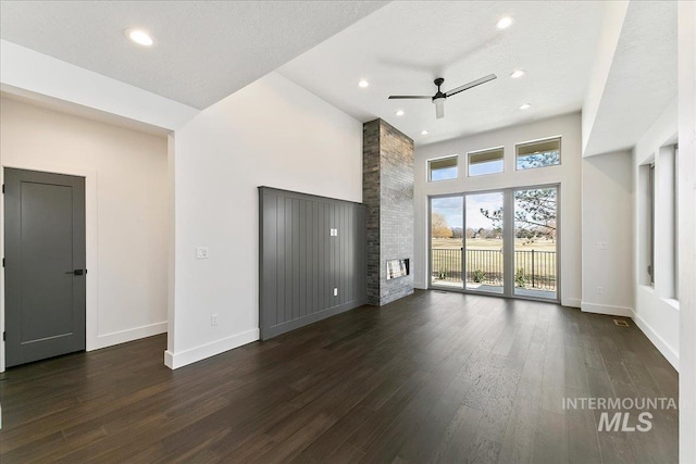 unfurnished living room featuring a large fireplace, baseboards, and dark wood finished floors