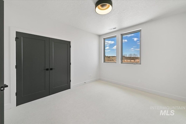 unfurnished bedroom featuring visible vents, baseboards, a textured ceiling, carpet flooring, and a closet