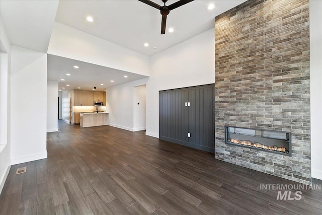 unfurnished living room with dark wood finished floors, visible vents, a fireplace, and baseboards