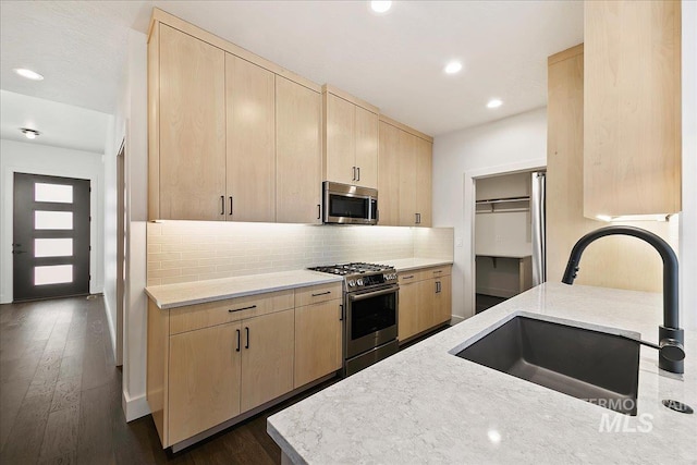 kitchen with appliances with stainless steel finishes, a sink, backsplash, and light brown cabinetry