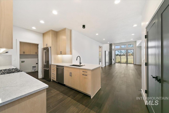 kitchen featuring a peninsula, stainless steel appliances, a sink, open floor plan, and light brown cabinetry