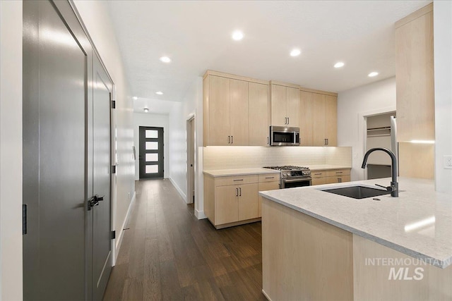 kitchen featuring stainless steel appliances, decorative backsplash, light brown cabinetry, dark wood-type flooring, and a sink