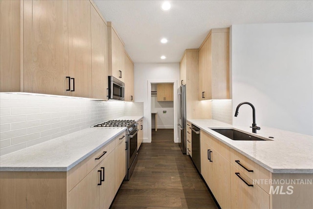 kitchen with appliances with stainless steel finishes, dark wood-type flooring, light brown cabinets, a sink, and a peninsula