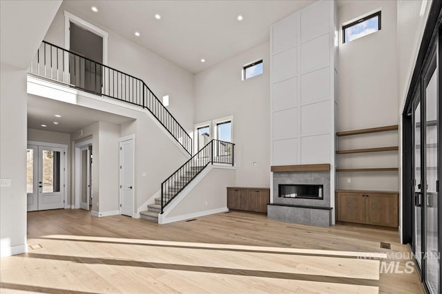 unfurnished living room featuring a towering ceiling, light hardwood / wood-style flooring, and a healthy amount of sunlight