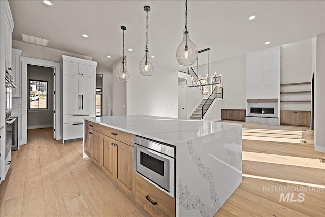 kitchen featuring a large island, light hardwood / wood-style flooring, white cabinetry, hanging light fixtures, and light stone counters