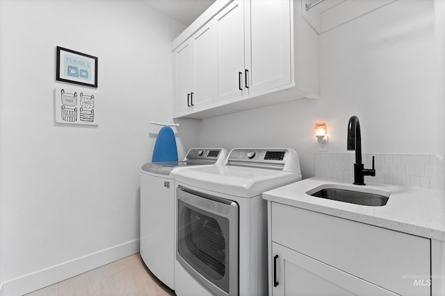 clothes washing area featuring washer and clothes dryer, cabinet space, baseboards, and a sink