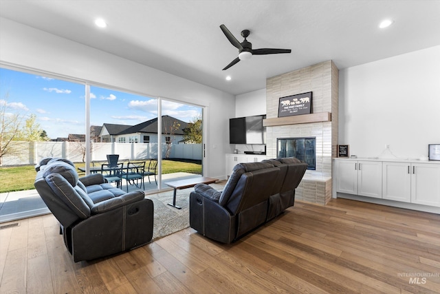living room with wood-type flooring, a brick fireplace, ceiling fan, and recessed lighting