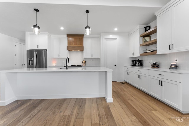 kitchen featuring white cabinetry, open shelves, premium range hood, stainless steel fridge, and backsplash