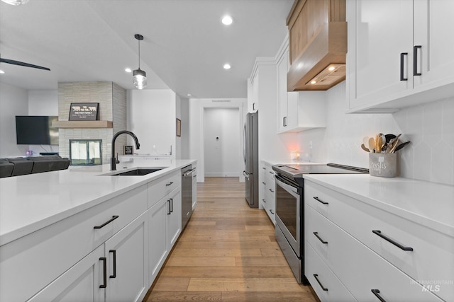 kitchen with stainless steel appliances, a sink, light wood-type flooring, backsplash, and wall chimney range hood