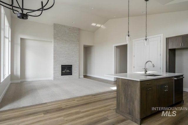 kitchen featuring a center island with sink, a stone fireplace, carpet flooring, and sink