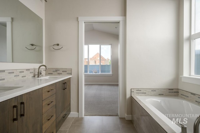 bathroom featuring tile patterned flooring, vaulted ceiling, backsplash, tiled bath, and vanity