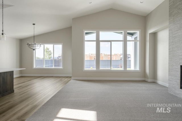 unfurnished living room with light hardwood / wood-style floors, a stone fireplace, an inviting chandelier, and lofted ceiling