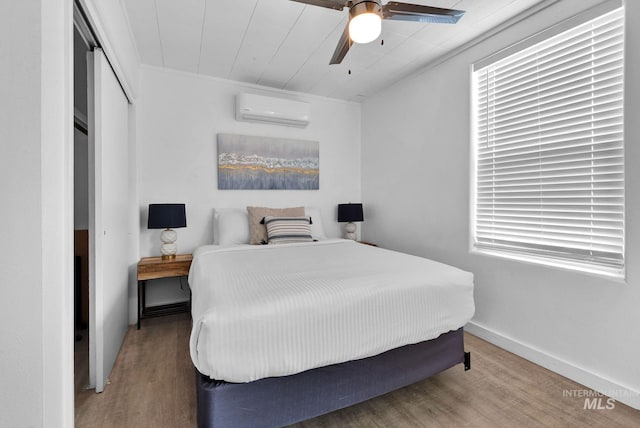 bedroom featuring a closet, a wall mounted AC, wood finished floors, and baseboards