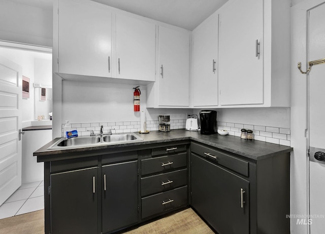 kitchen featuring tasteful backsplash, dark countertops, white cabinets, and a sink