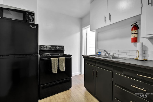 kitchen with dark countertops, decorative backsplash, white cabinetry, a sink, and black appliances