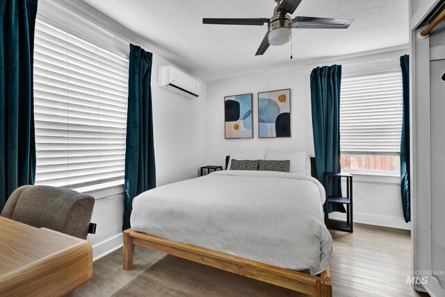 bedroom featuring a wall unit AC, ceiling fan, baseboards, and wood finished floors