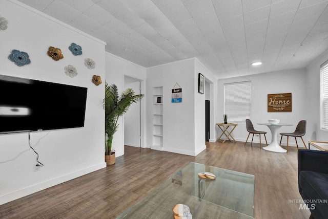 living room featuring baseboards, crown molding, built in features, and wood finished floors