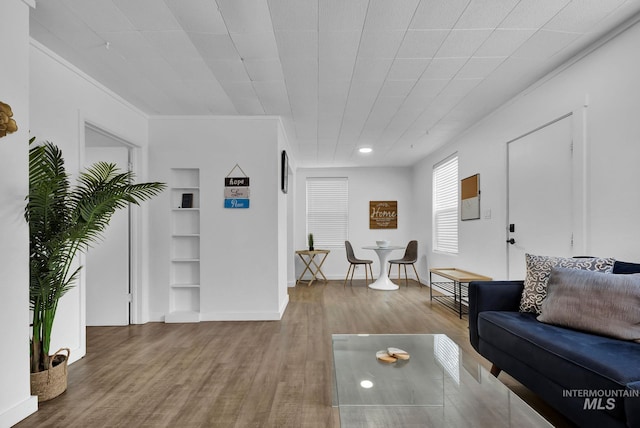 living room featuring built in shelves, ornamental molding, baseboards, and wood finished floors