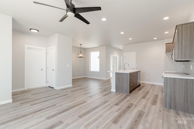 4435 N Magical Creek Ave, Meridian, ID 83646 - kitchen featuring light wood-type flooring, an island with sink, ceiling fan, light countertops, and baseboards