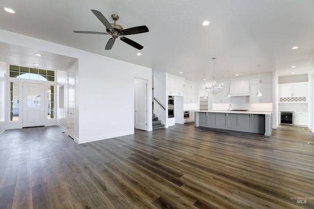 unfurnished living room with ceiling fan with notable chandelier, dark hardwood / wood-style floors, wine cooler, and sink