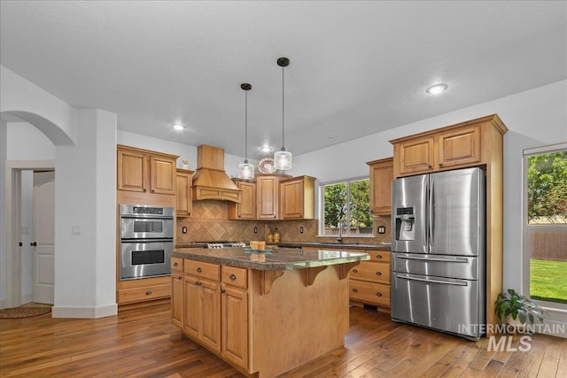 6370 E Escarpment Ct, Boise, ID 83716 - kitchen featuring appliances with stainless steel finishes, custom range hood, a kitchen island, arched walkways, and dark wood-style flooring