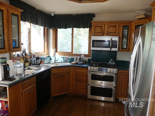 kitchen featuring dark wood finished floors, brown cabinetry, dark countertops, appliances with stainless steel finishes, and a sink