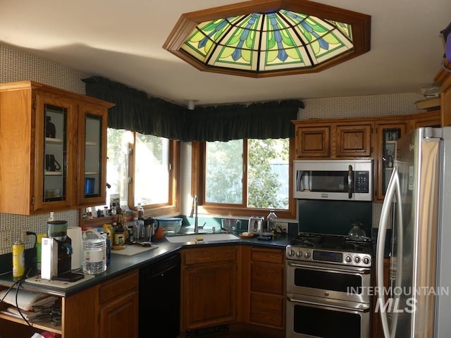 kitchen featuring brown cabinetry, dark countertops, glass insert cabinets, stainless steel appliances, and a sink