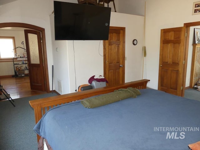 bedroom with a wainscoted wall, visible vents, arched walkways, and wood finished floors