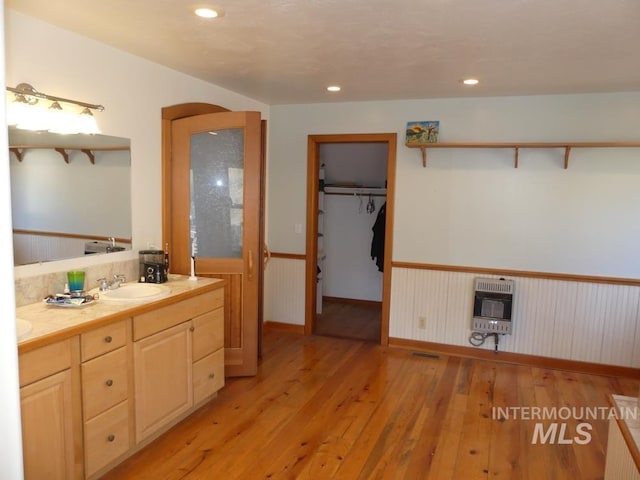 full bathroom featuring a sink, wainscoting, heating unit, double vanity, and wood-type flooring