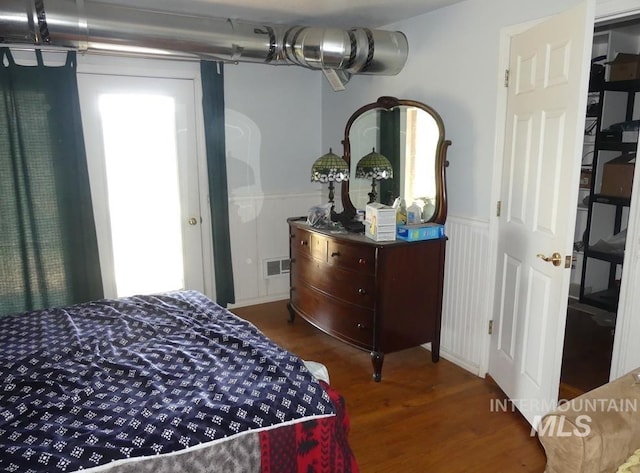 bedroom featuring a wainscoted wall, visible vents, and wood finished floors