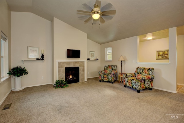 living area with a ceiling fan, visible vents, lofted ceiling, a tile fireplace, and carpet flooring