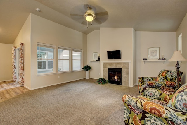 carpeted living room with baseboards, lofted ceiling, a ceiling fan, and a tiled fireplace