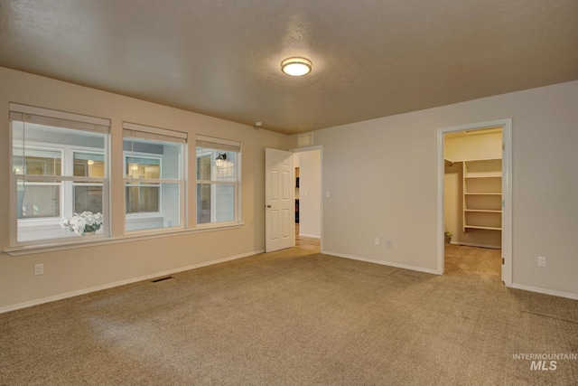 empty room featuring a textured ceiling, carpet, visible vents, and baseboards