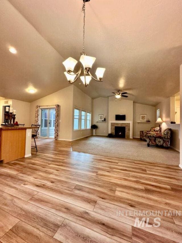 unfurnished living room featuring a fireplace, vaulted ceiling, ceiling fan with notable chandelier, and light wood finished floors