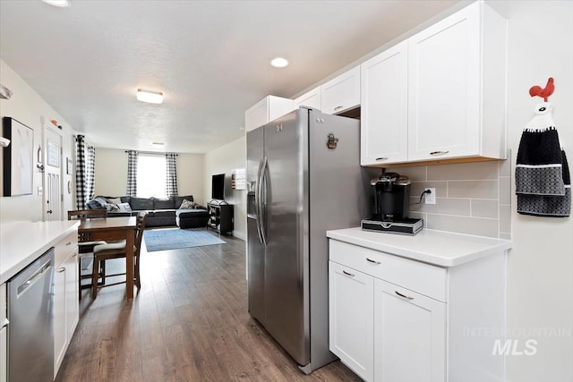 kitchen with white cabinets, dark wood finished floors, appliances with stainless steel finishes, open floor plan, and backsplash