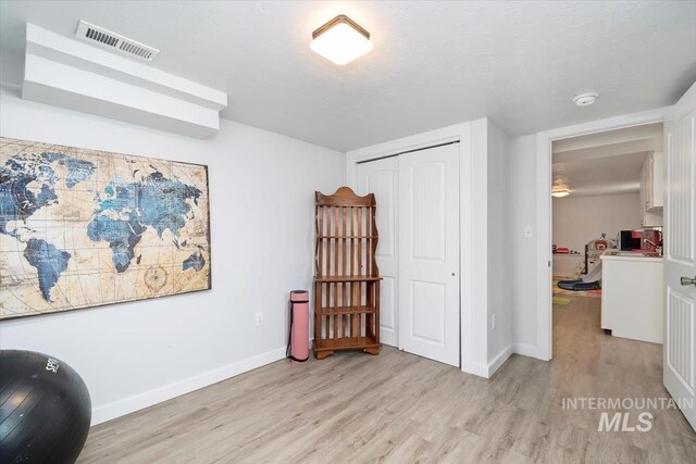 interior space featuring baseboards, a textured ceiling, visible vents, and light wood finished floors