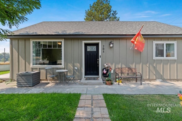 view of front facade with a shingled roof, a patio area, and board and batten siding