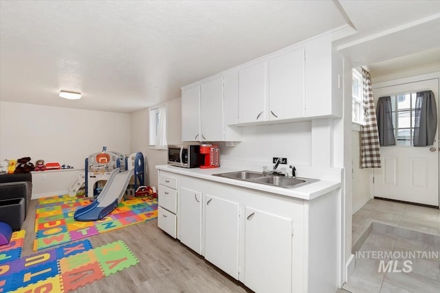 kitchen with light countertops, white cabinets, stainless steel microwave, a sink, and light wood-style floors