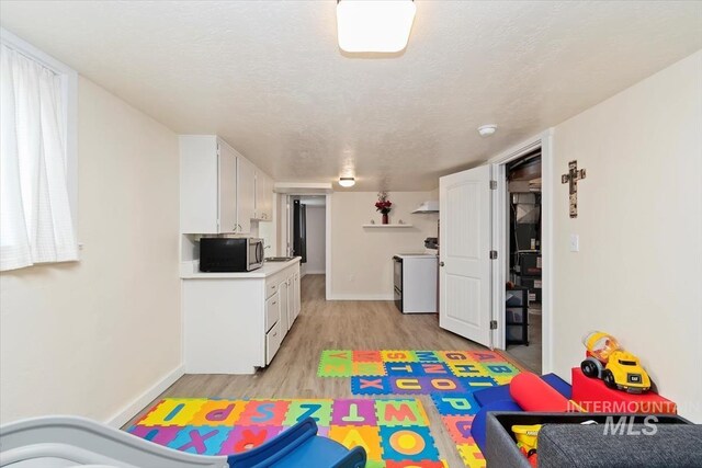 recreation room featuring baseboards, a textured ceiling, and light wood-style flooring