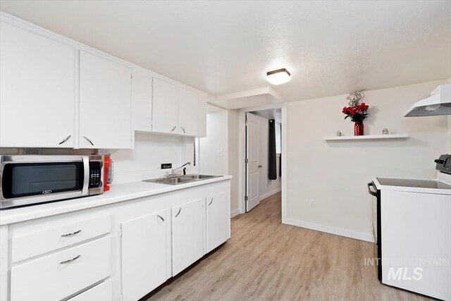kitchen featuring light countertops, light wood finished floors, stainless steel microwave, a sink, and range with electric stovetop