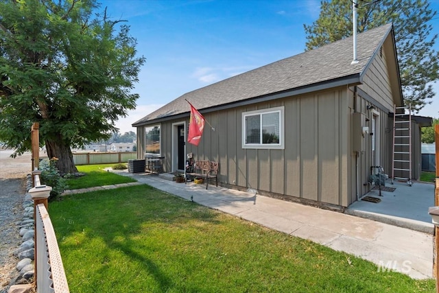 rear view of property featuring fence, central AC unit, board and batten siding, roof with shingles, and a lawn