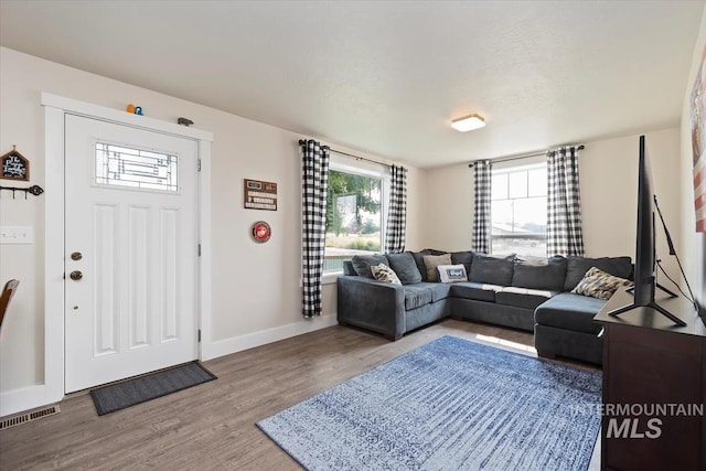 living area featuring baseboards, visible vents, a textured ceiling, and wood finished floors