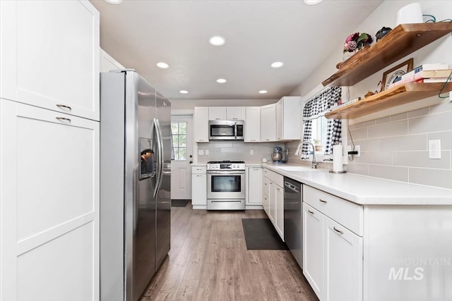 kitchen with white cabinets, appliances with stainless steel finishes, a sink, light wood-style floors, and backsplash