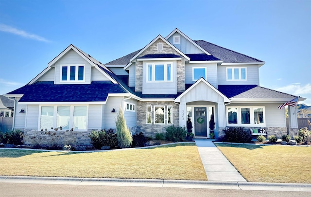 craftsman house featuring board and batten siding, stone siding, a shingled roof, and a front lawn