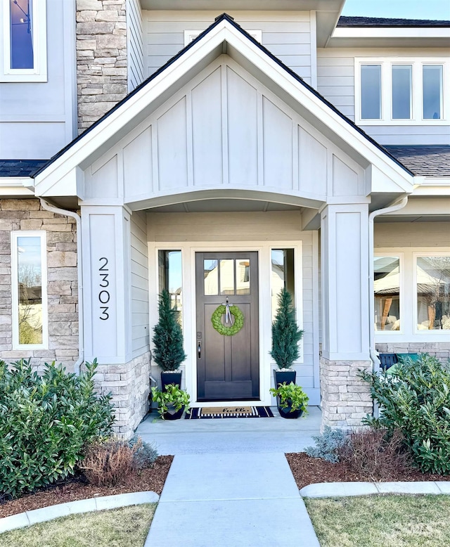 doorway to property with stone siding, a shingled roof, and board and batten siding