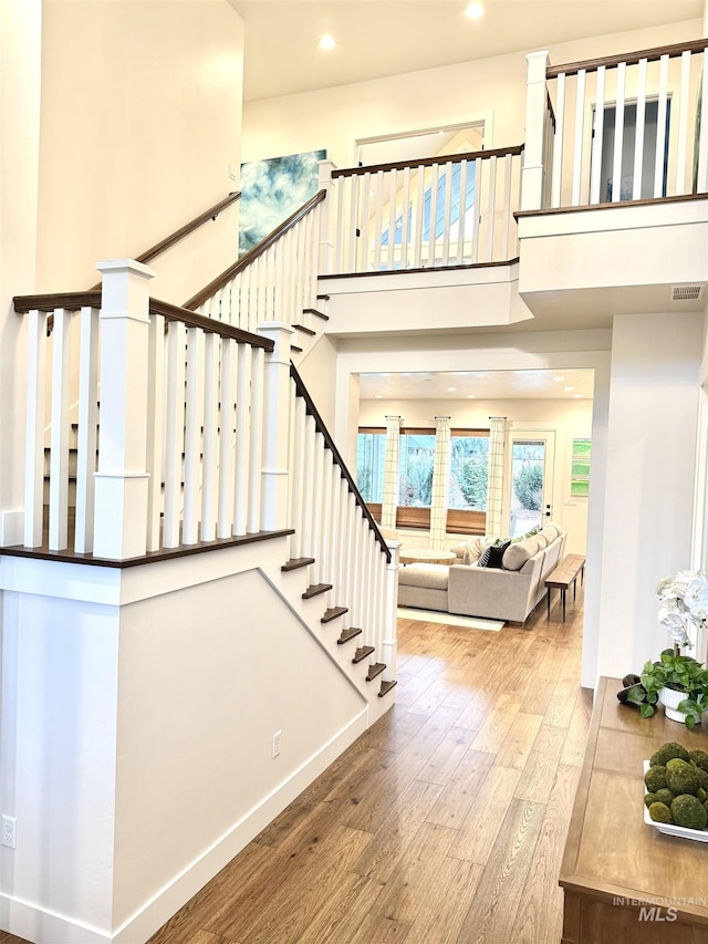 staircase featuring recessed lighting, a high ceiling, wood finished floors, visible vents, and baseboards