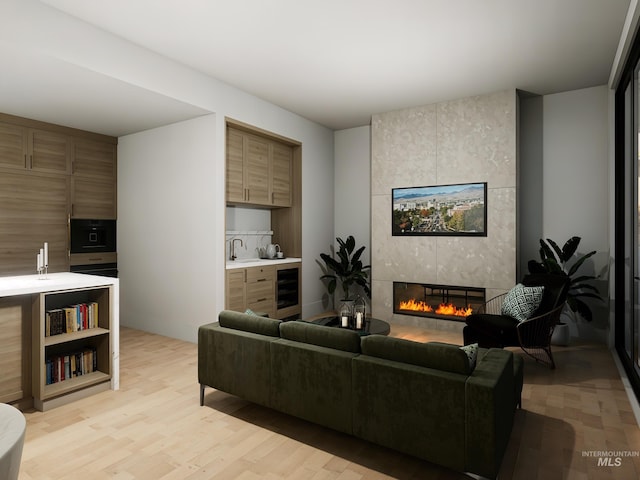 living area featuring beverage cooler, light wood-style flooring, and a tiled fireplace