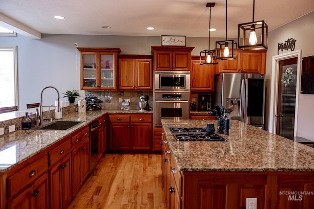 kitchen featuring pendant lighting, sink, light wood-type flooring, light stone counters, and stainless steel appliances